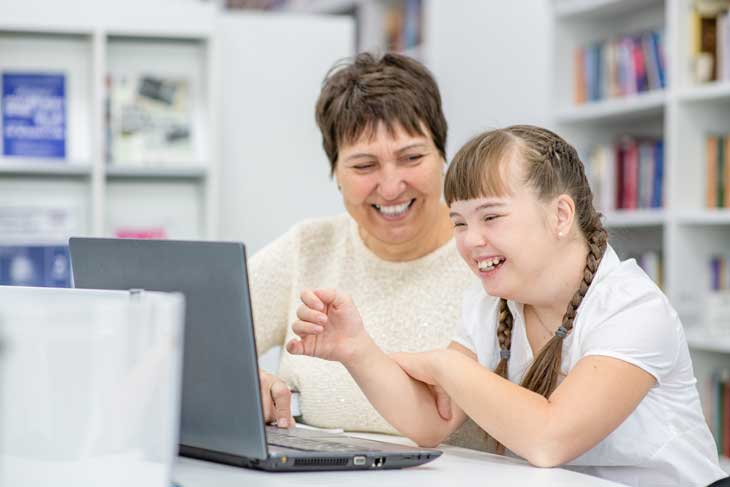 Child with disability being supported by teacher to learn on laptop