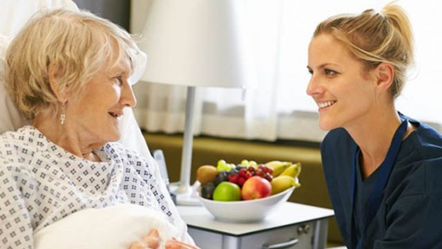 A female nurse conversing happily with an elderly lady at her bedside