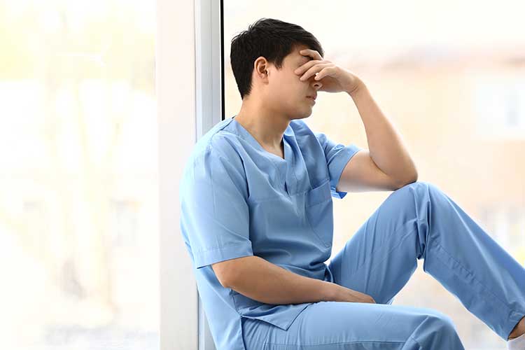 Male nurse sitting by a windowsill looking stressed and tired