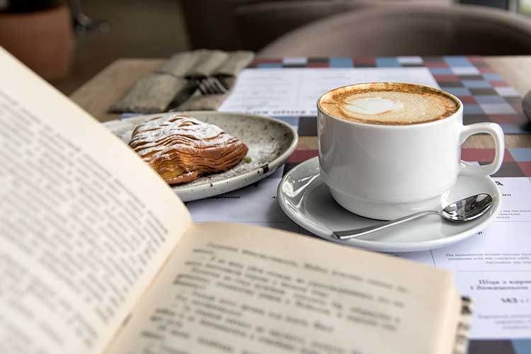A cappuccino, almond croissant and book lying on a table