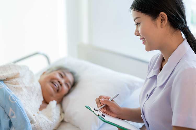 A female nurse looking happily at a female elderly patient lying on her bed
